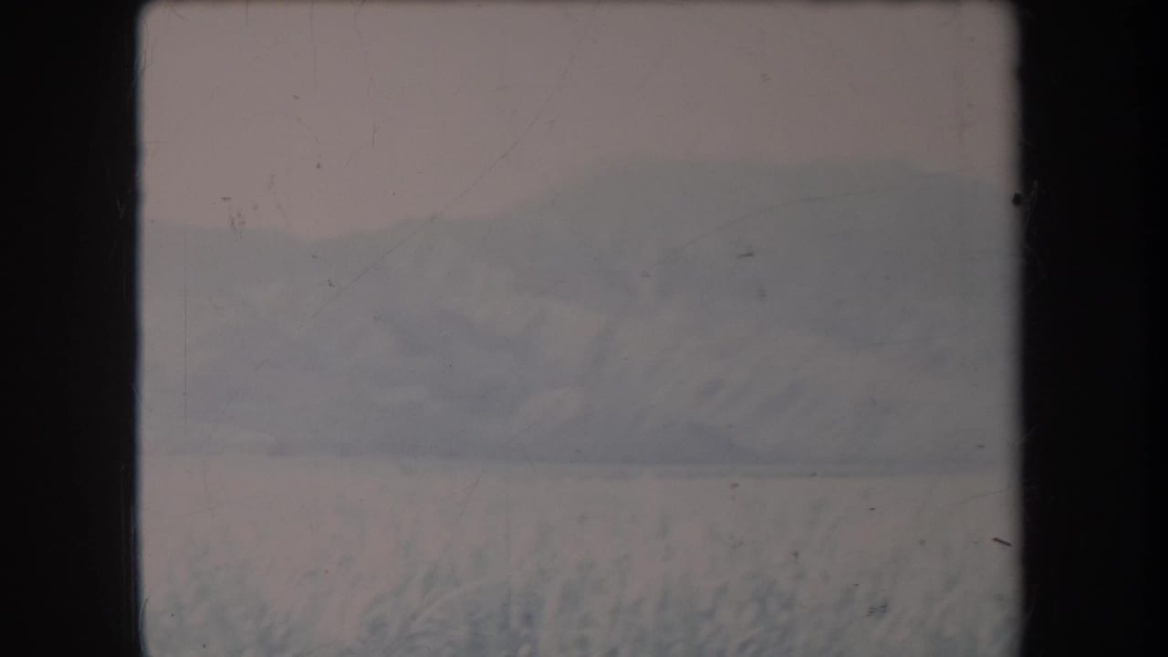 1969 Hawaii home-movie frame with snow in the foreground and a faded mountain range across the horizon.