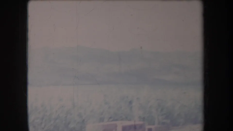 1969 Hawaii 8mm frame showing a pale crop field, hazy mountains, and a small indistinct structure at the bottom of the view.