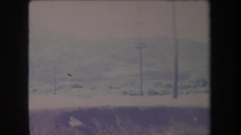 Hazy 1969 Hawaii landscape with distant rolling hills, utility poles, power lines, and a pale roadside strip in a faded 8mm frame.
