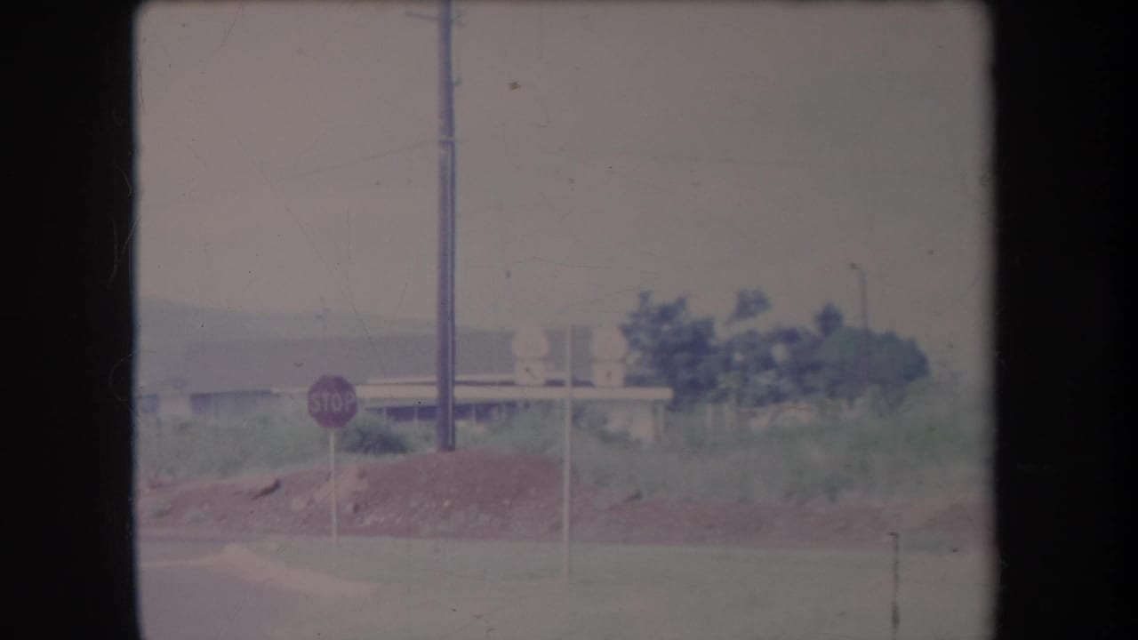 1969 Hawaii roadside view with a red stop sign, utility pole, dirt mound, low building, and green vegetation.