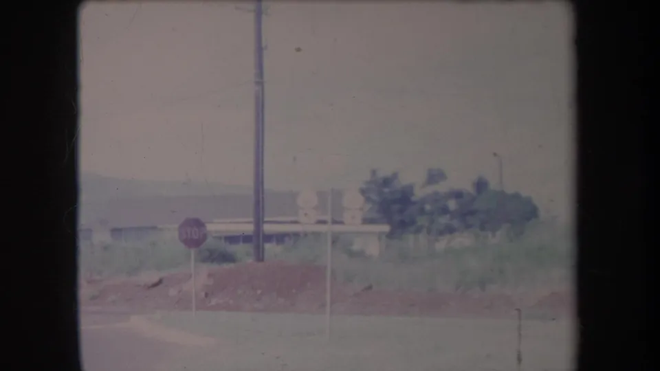 1969 Hawaii roadside view with a red stop sign, utility pole, dirt mound, low building, and green vegetation.