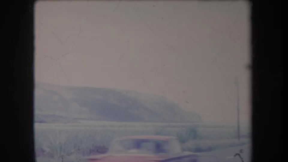 1969 Hawaii 8mm frame showing a hazy rural landscape, low scrub, distant hills and a dark window or film-frame edge.