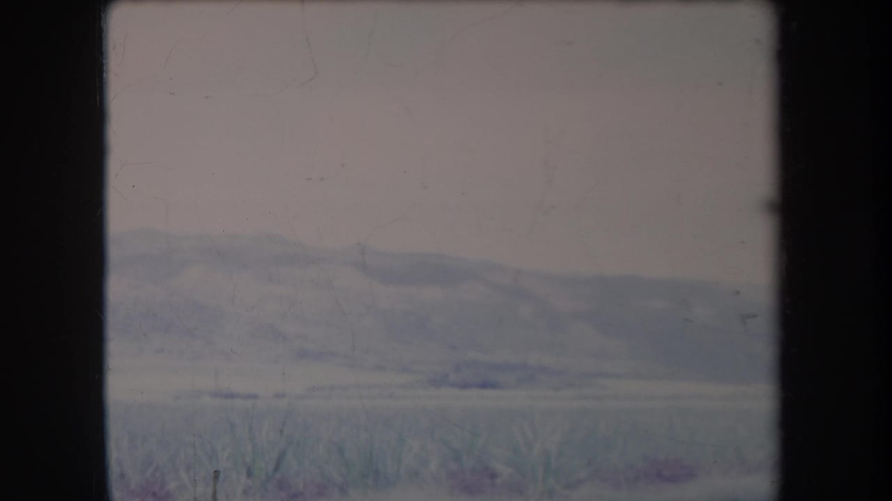 1969 Hawaii home-movie frame with soft, hazy hills, pale sky and low vegetation in a faded 8mm landscape view.