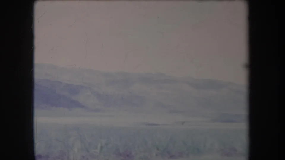 Faded 1969 Hawaii 8mm frame of a quiet rural landscape with distant hills, scrub vegetation and visible film wear.