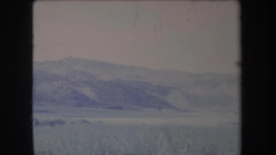 1969 Hawaii travel-film frame showing hazy rolling hills, low vegetation, pale sky and dark vertical borders from the filmed view.