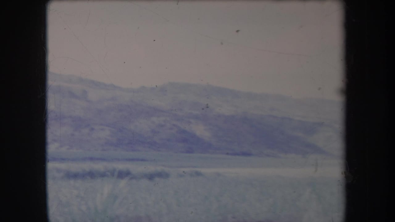 1969 Hawaii 8mm frame showing distant hills, open grassy land, and foreground grass through a soft, faded film scan.