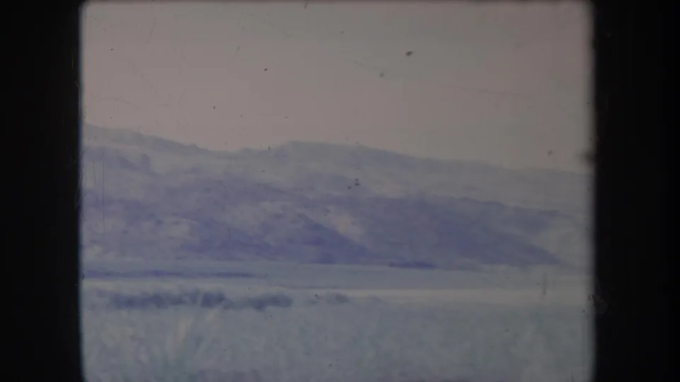 1969 Hawaii 8mm frame showing distant hills, open grassy land, and foreground grass through a soft, faded film scan.