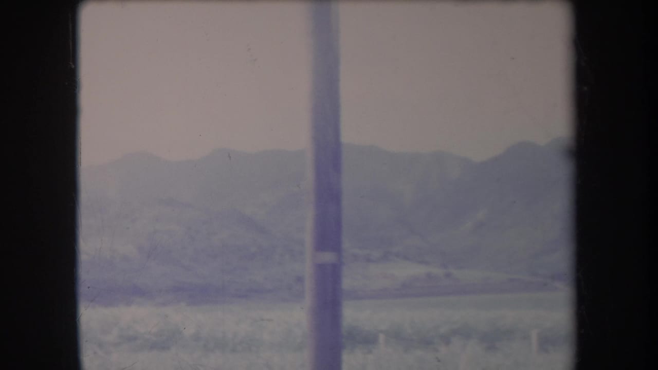 Hazy mountains and brush seen through dark vertical framing with a pole near the center.