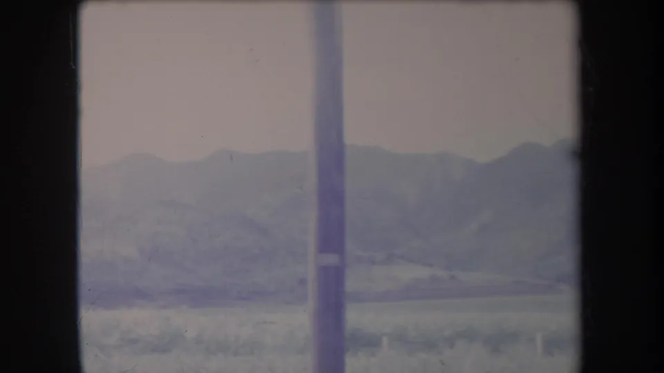 1969 Hawaii 8mm frame showing distant hazy mountains, pale sky, scrub vegetation, and a vertical pole through a dark foreground frame.