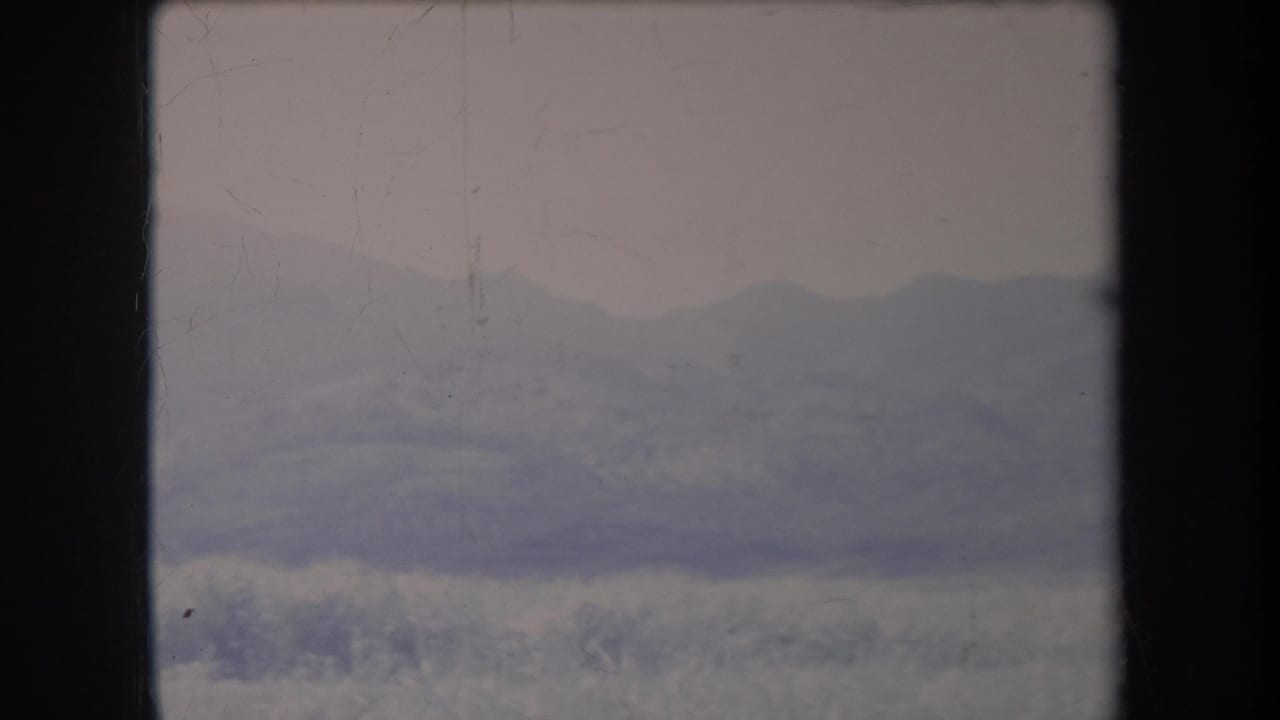 1969 Hawaii home-movie still of a hazy mountain ridge and low grassy foreground, partly bordered by dark window or film-frame edges.