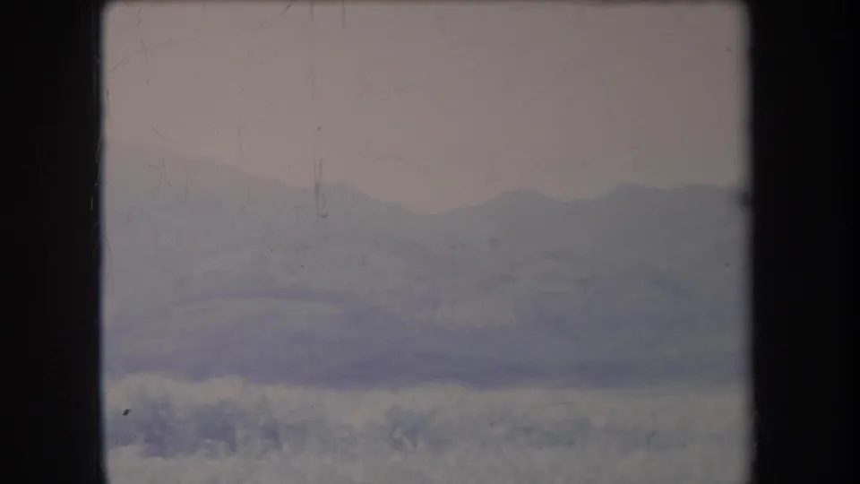 1969 Hawaii home-movie still of a hazy mountain ridge and low grassy foreground, partly bordered by dark window or film-frame edges.