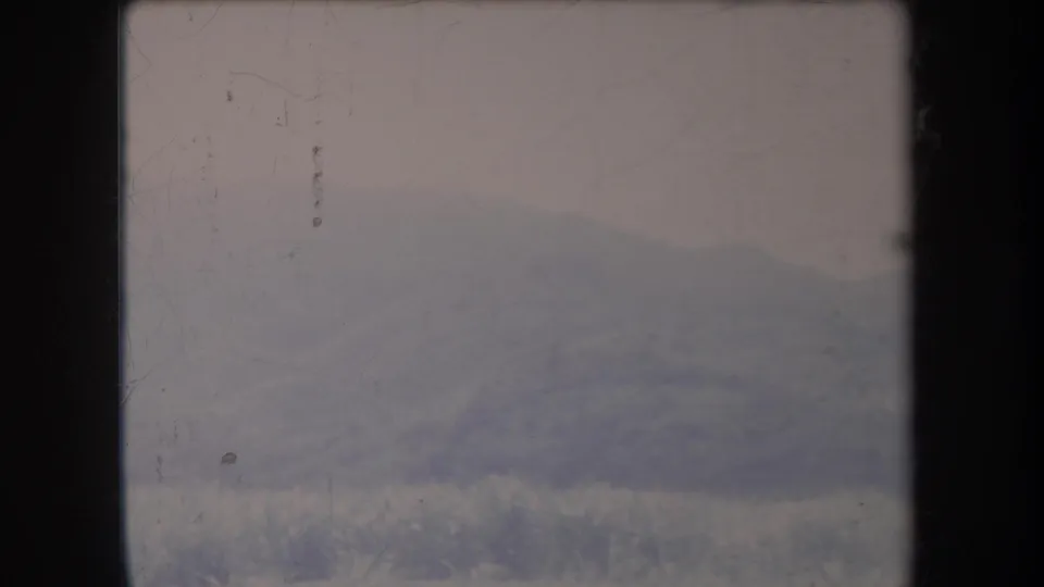 Muted 1969 Hawaii 8mm view of fog-softened mountains and foreground vegetation seen through dark vertical framing.