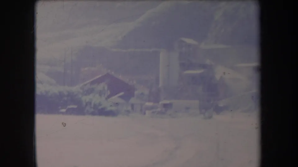 1969 Hawaii 8mm frame showing a distant rural farm scene with buildings, posts, open land, and hazy hillside terrain.