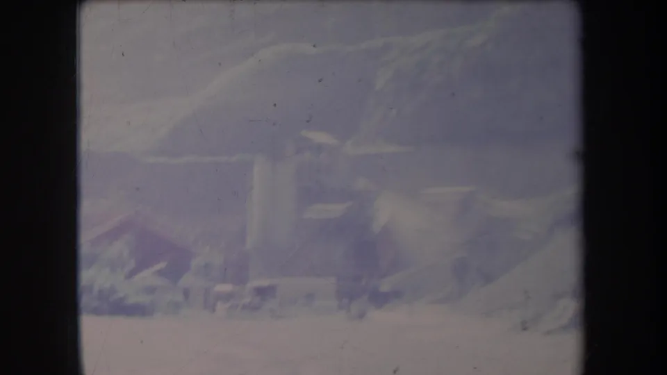 1969 Hawaii 8mm frame showing hazy hills, foliage, and a distant structure under a pale sky with visible film wear.