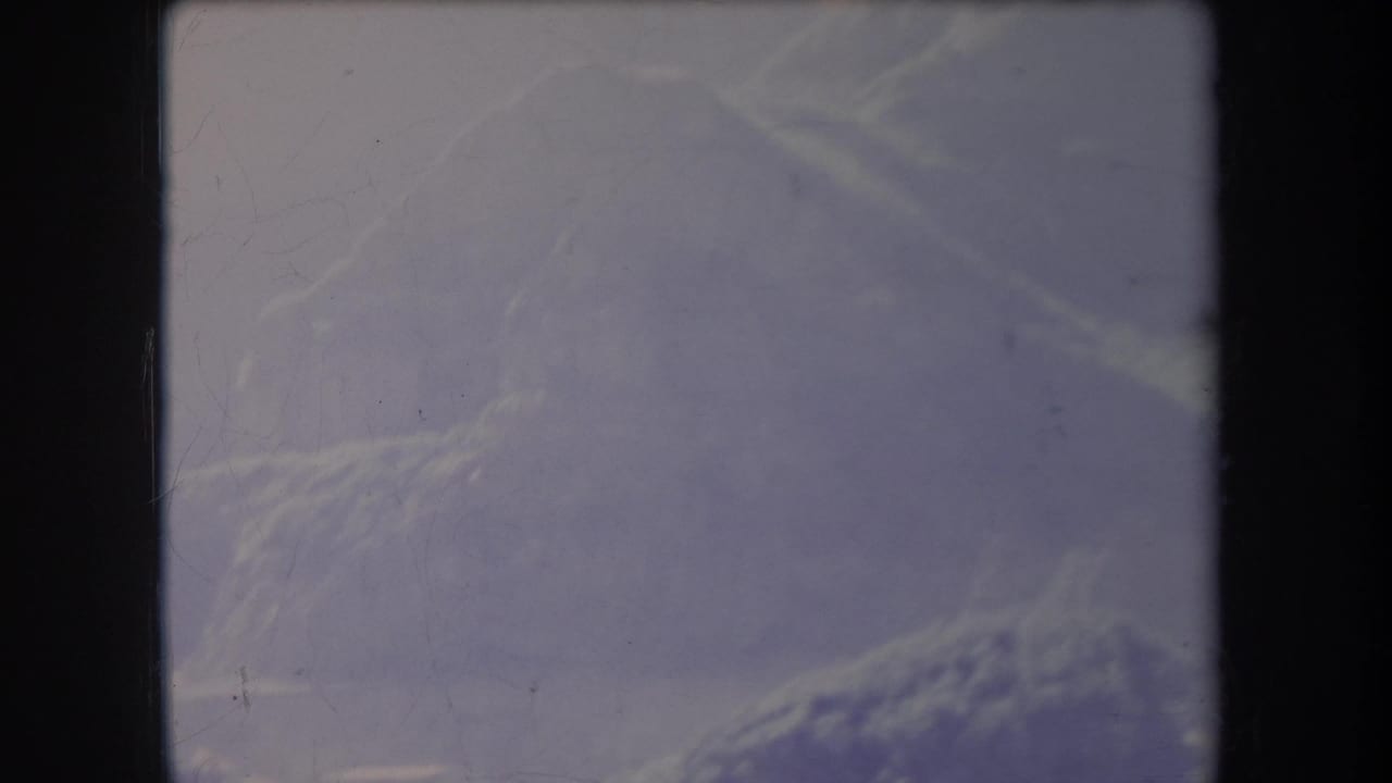 Faded mountain slope and pale sky seen through scratched film.