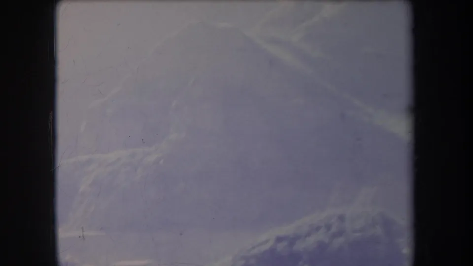 1969 Hawaii landscape frame with soft mountain contours, pale sky, purple color cast, and visible 8mm film scratches.