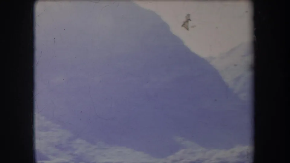 1969 Hawaii landscape frame with a broad hillside silhouette, pale sky, faint foliage texture, and worn 8mm film surface.
