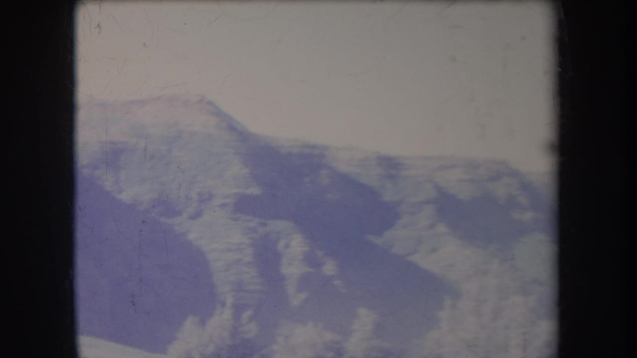 Soft, faded mountain ridges beneath a pale sky within a dark film frame.