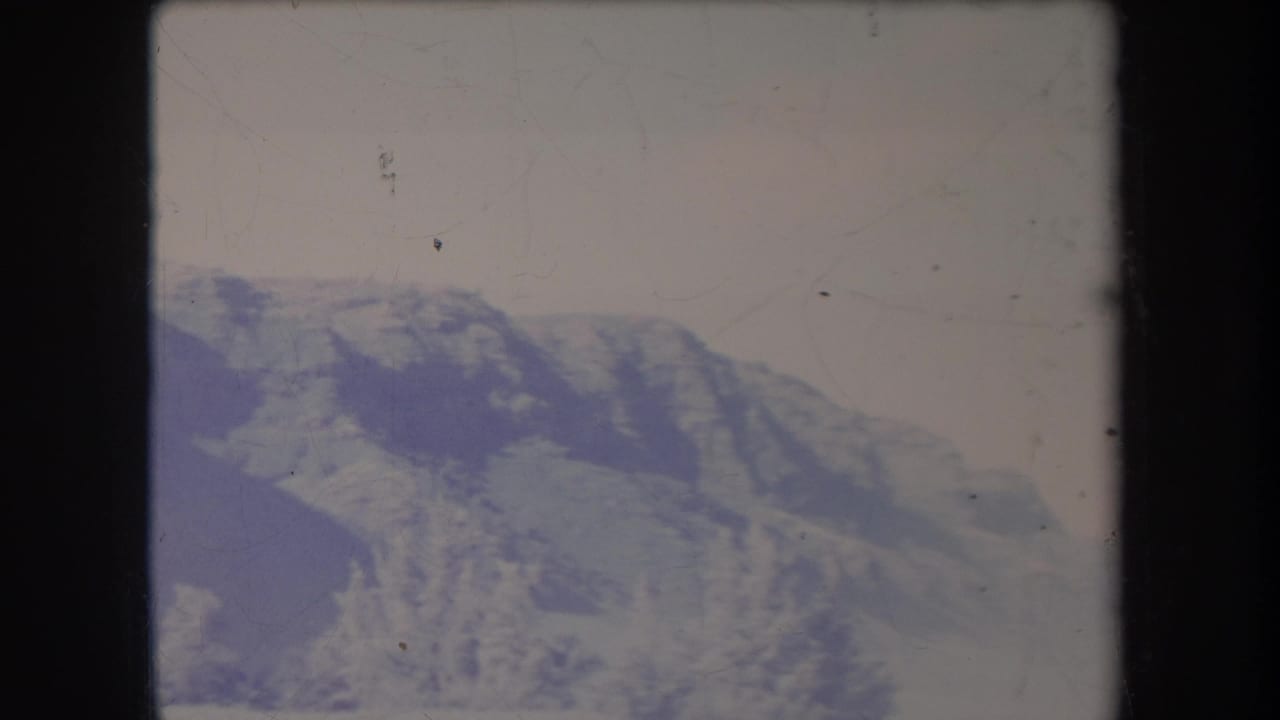 Hazy 1969 Hawaii mountain landscape in a soft 8mm frame, with ridges, pale sky, and archival surface wear visible.