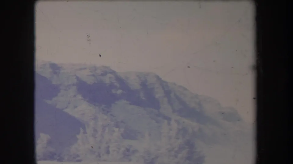 Hazy 1969 Hawaii mountain landscape in a soft 8mm frame, with ridges, pale sky, and archival surface wear visible.