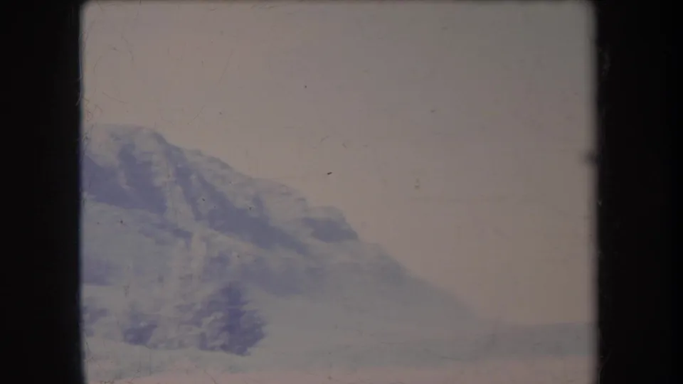Faded 8mm view of a Hawaii mountain slope and valley edge, with soft focus, pale sky, and visible frame wear.