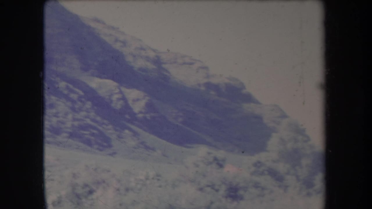 Snow-dusted mountain ridge under a pale sky with dark film borders.