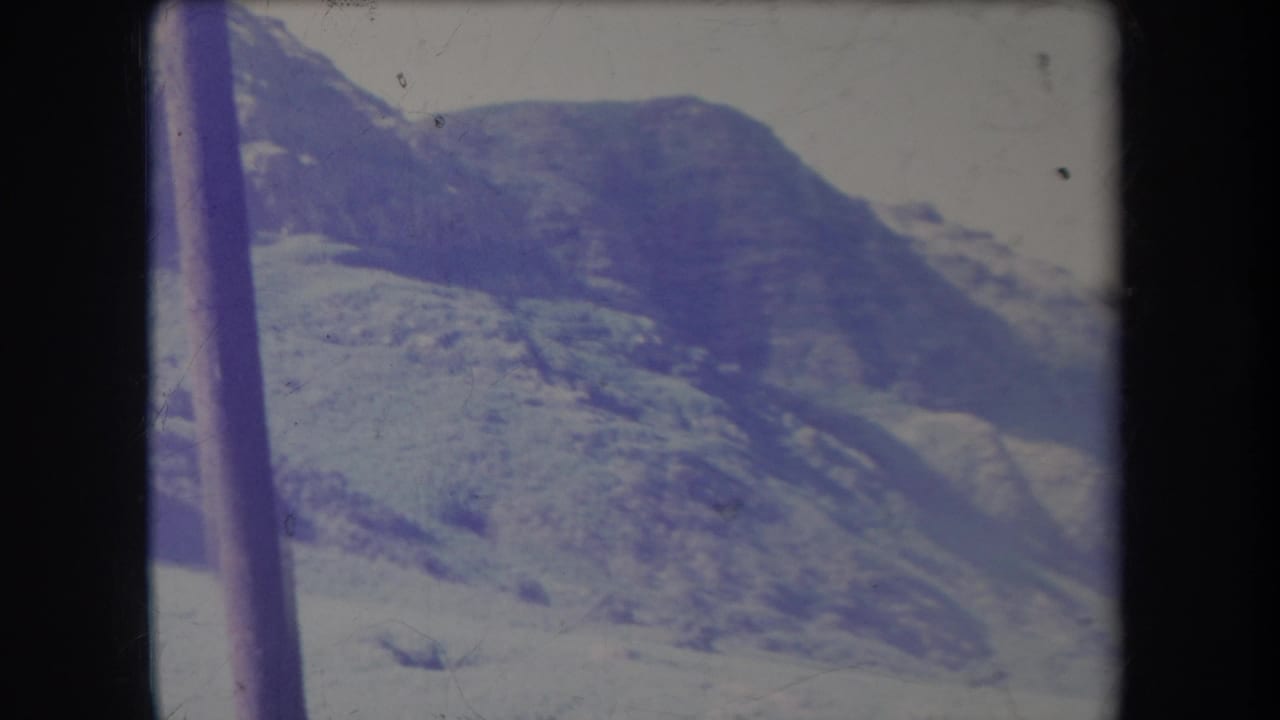 1969 Hawaii 8mm frame of snow-marked mountain terrain, with a dark vertical pole crossing the foreground and faded blue color.