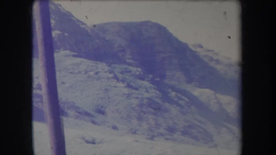 1969 Hawaii 8mm frame of snow-marked mountain terrain, with a dark vertical pole crossing the foreground and faded blue color.