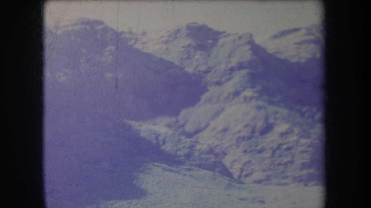 1969 Hawaii 8mm frame showing hazy mountain terrain, a distant coastline, soft focus, and visible film wear.