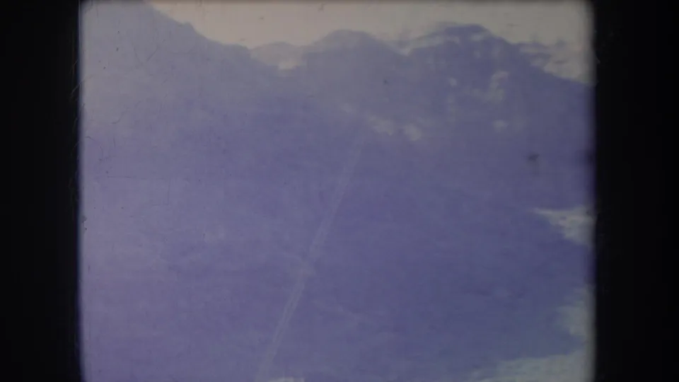 1969 Hawaii home-movie frame with layered mountain silhouettes, muted terrain detail, and aged 8mm scratches.