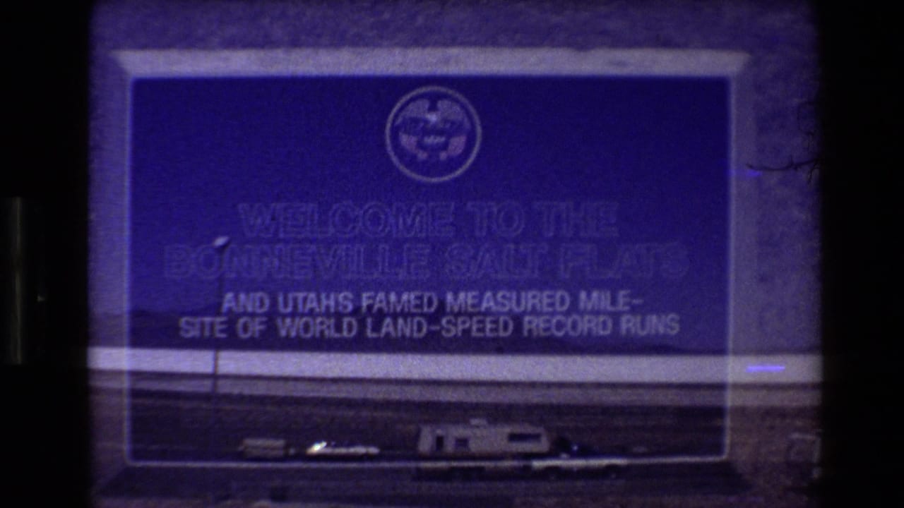 1980 8mm frame showing a Bonneville Salt Flats welcome sign above parked vehicles at the edge of the flats.