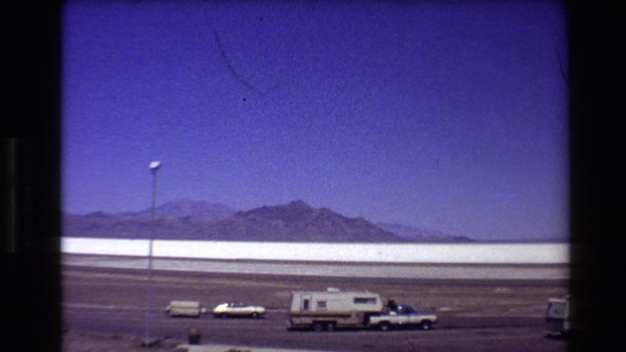 Wide 1980 Bonneville Salt Flats view with a pickup, camper trailer, and car parked below a deep blue sky.