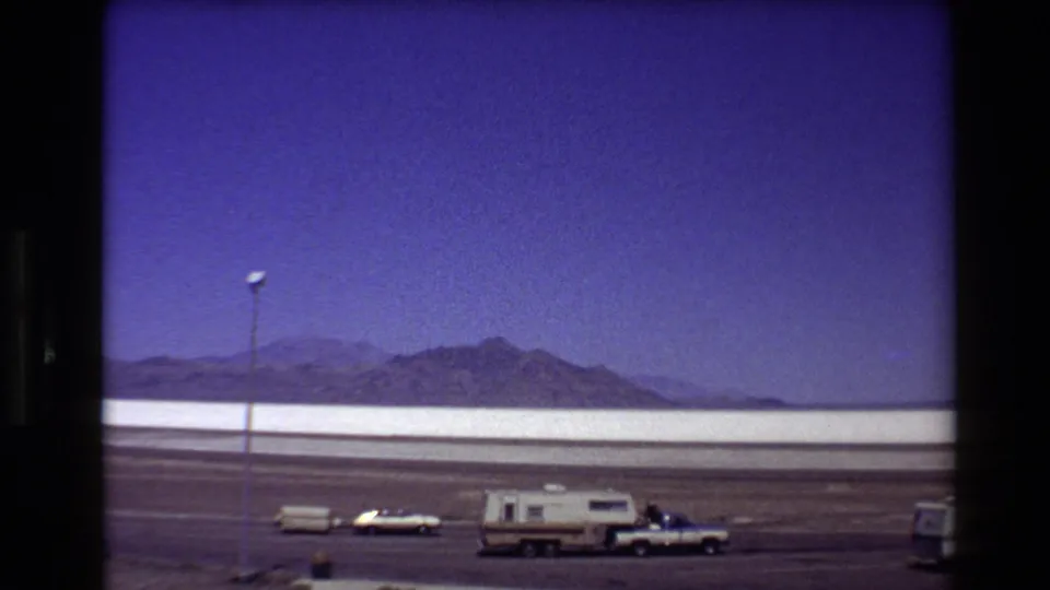 Home-movie view of parked recreational vehicles beside the Bonneville Salt Flats, with mountains across the horizon.