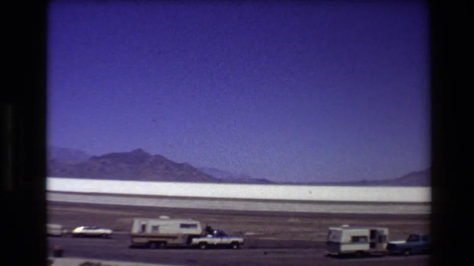 Wide Bonneville Salt Flats frame with camper trailers, a pickup, and cars parked against the white flats and distant mountains.