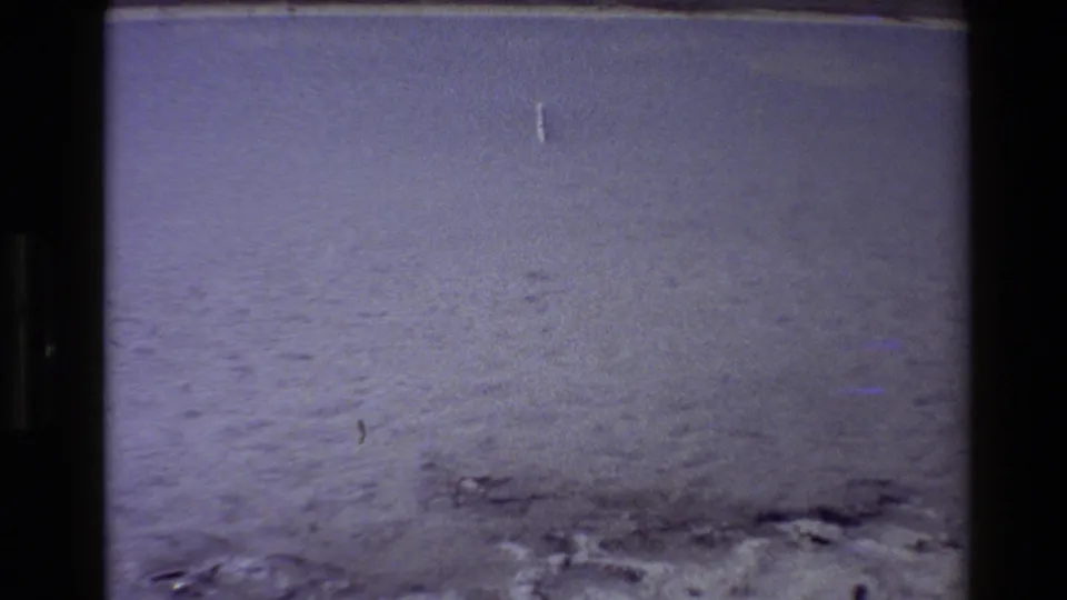 1980 Western USA 8mm frame showing flat snow or frost with faint footprints, small surface marks, and dark film borders.