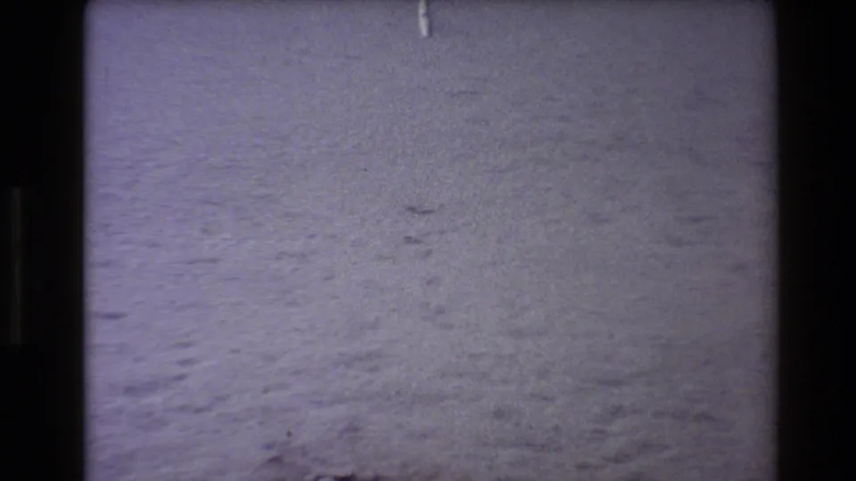 1980 Western USA 8mm frame of a pale snowy or frosty ground surface with faint tracks and grainy purple-tinted film texture.