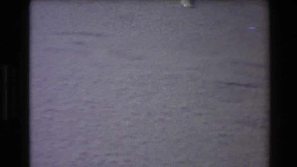 1980 Western USA 8mm frame with a pale winter ground surface, faint footprints or tracks, soft focus, and visible film-frame edges.