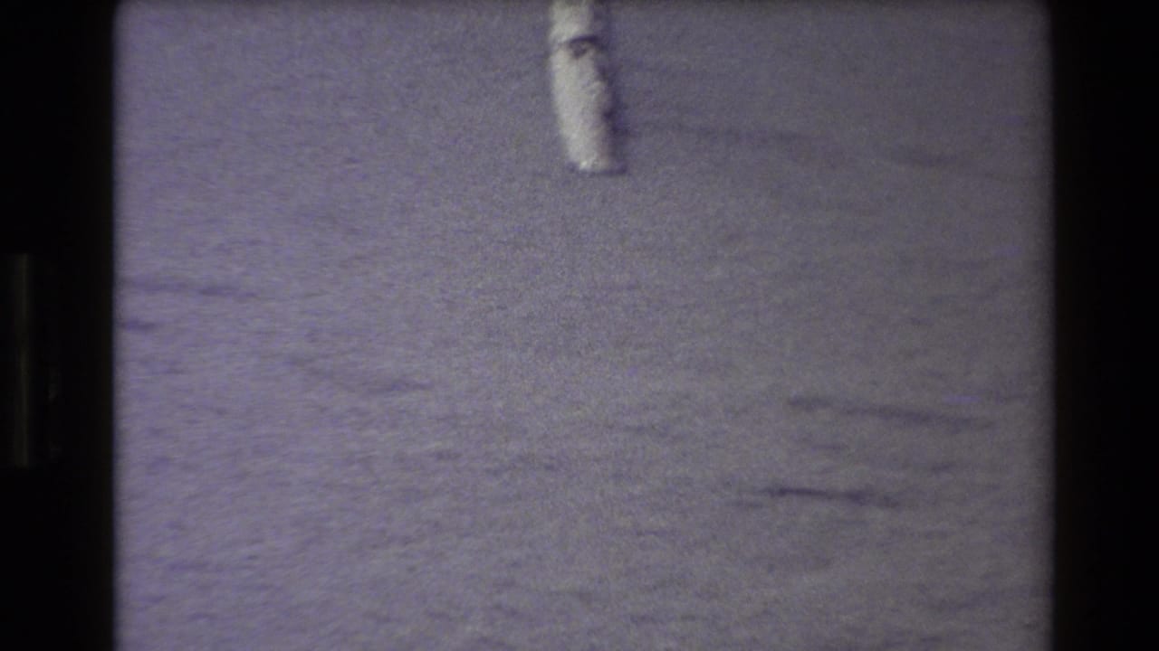 1980 Western USA 8mm frame showing a small pale object near the top edge on grainy sand with purple color shift and film-frame borders.