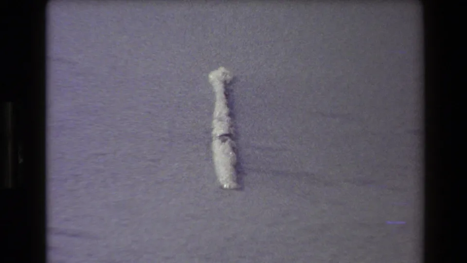 1980 Western USA 8mm frame showing the pale object lower in the frame on textured sand, with visible film borders and muted color shift.