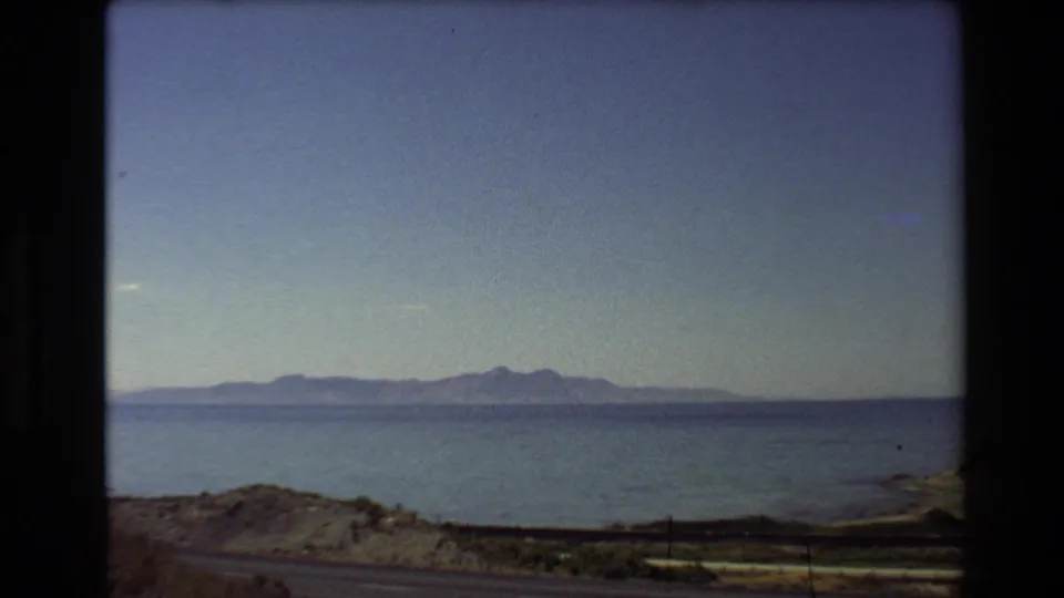 1980 Western U.S. home-movie frame showing a broad freshwater body, low shoreline, distant mountains, and blue sky from a moving vehicle.