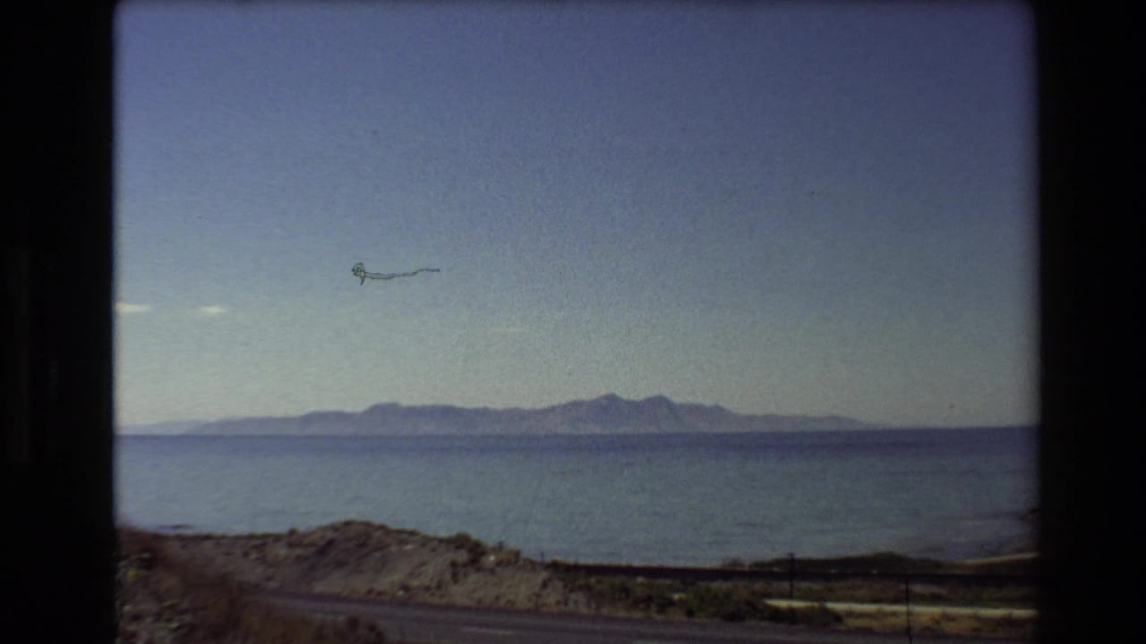 Lake and mountains under blue sky, with a small kite-like shape above the water.