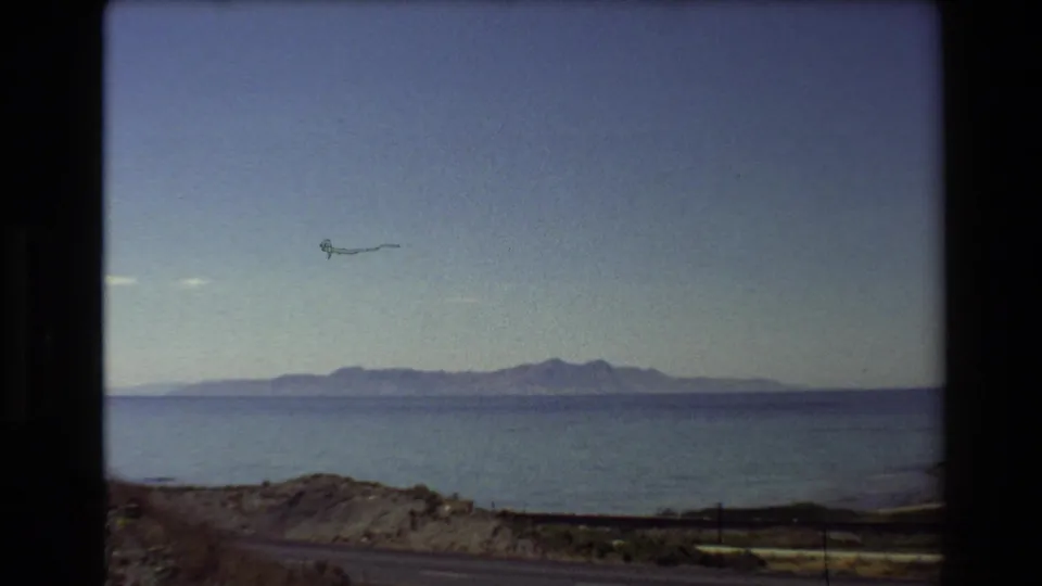 Western U.S. 1980 home-movie view of a lake, mountain horizon, roadside foreground, and a small kite-like object in the sky.