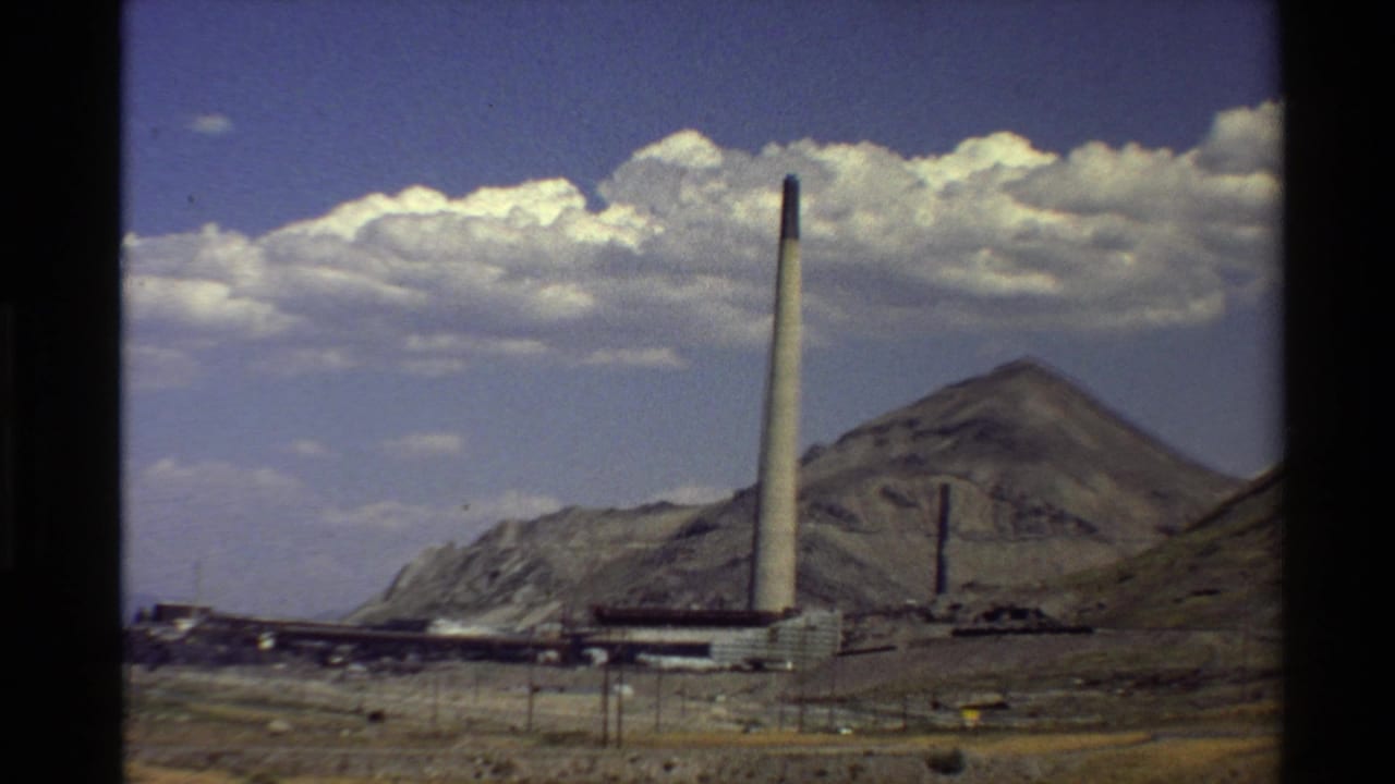 Factory smokestack and mountain landscape seen across dry ground.