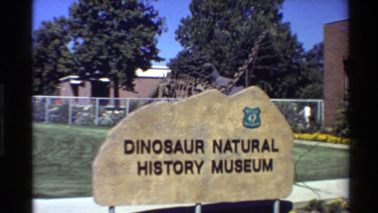 Brighter view of the museum sign with a dinosaur skeleton display visible behind a fence.