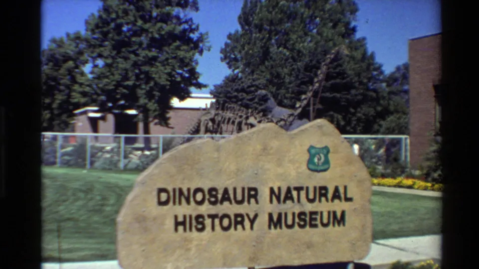 Final 8mm frame of the Dinosaur Natural History Museum sign outside a fenced exhibit area in the Western USA.