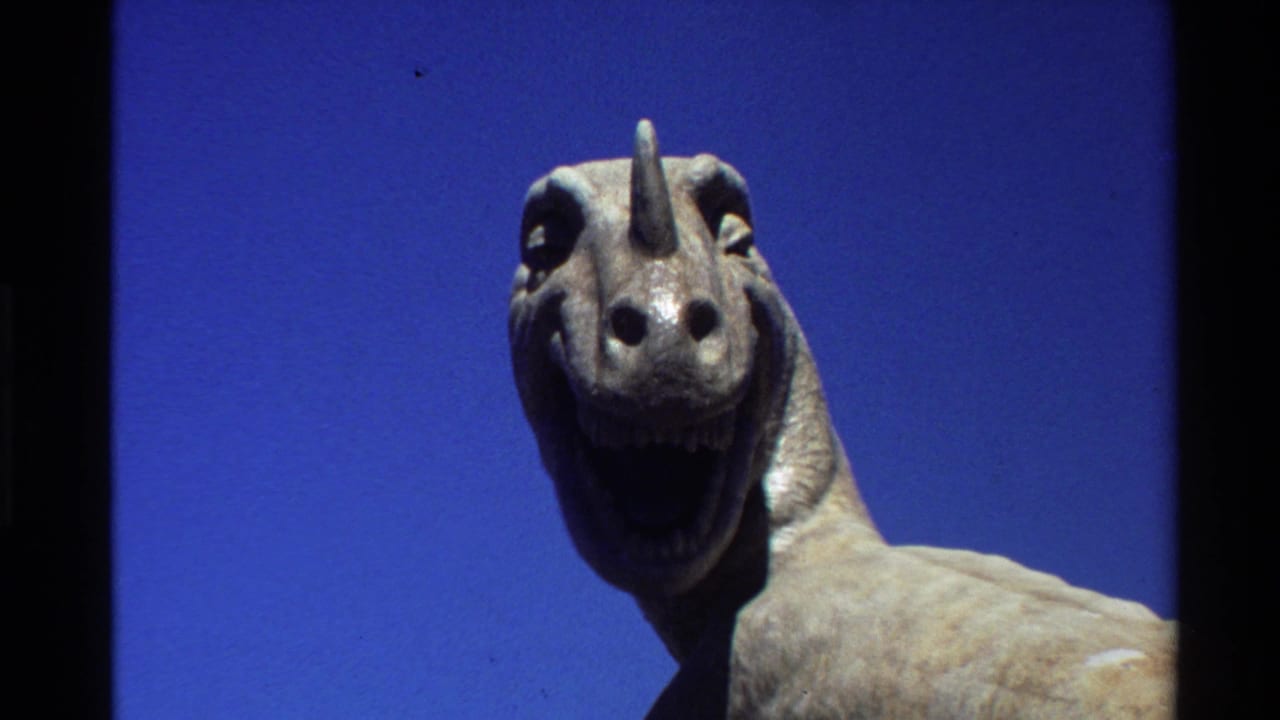 1980 Western U.S. 8mm frame showing a close horned dinosaur model head with an open mouth against clear blue sky.