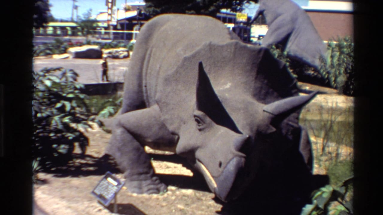 Outdoor triceratops model fills the frame with a parking area and buildings behind it.