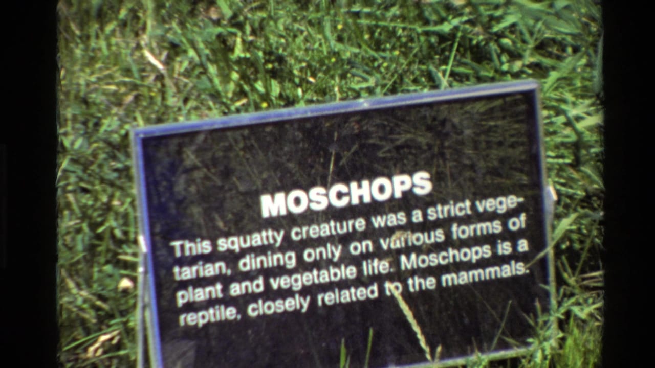 1980 Western USA 8mm frame showing a black Moschops informational sign in a grassy outdoor museum setting.
