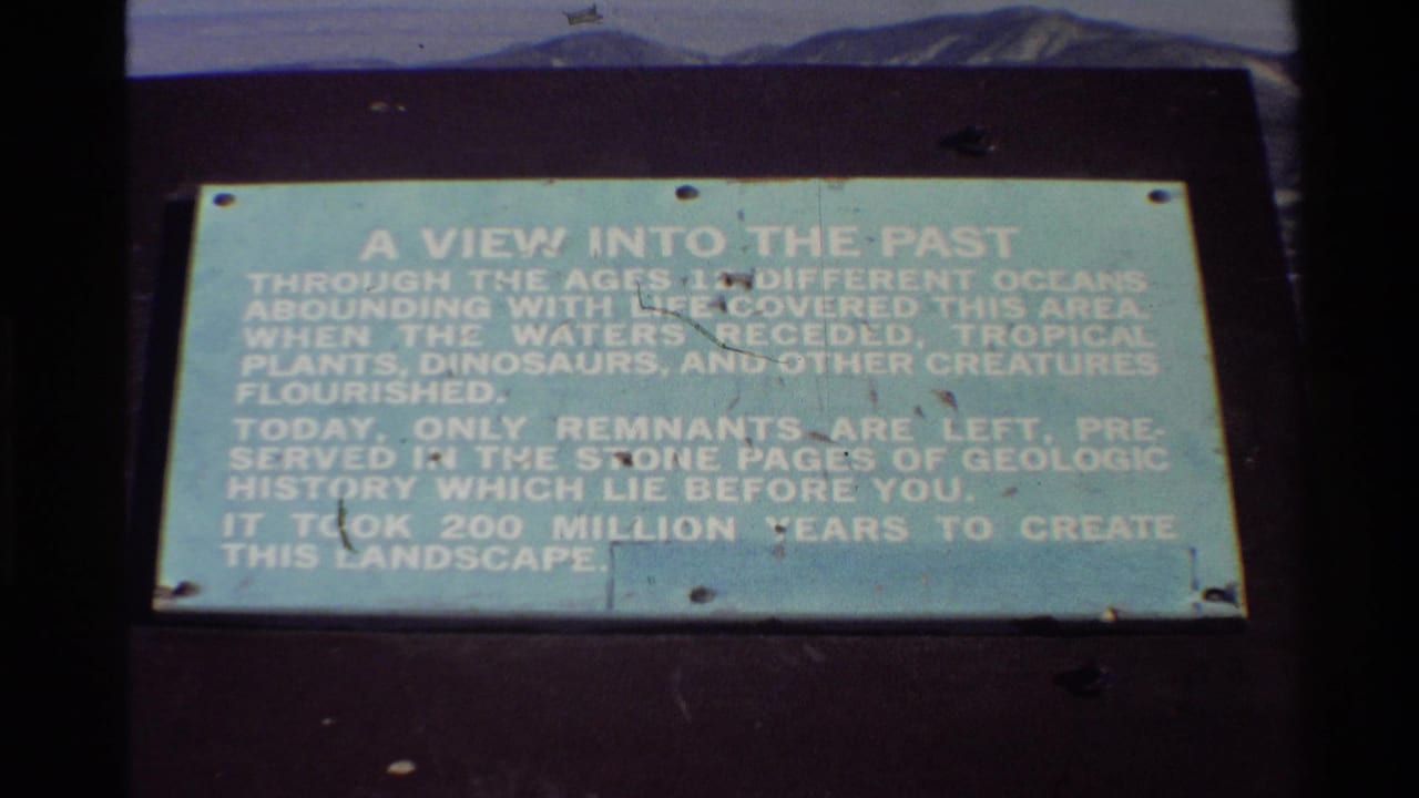 Outdoor informational plaque with white text about geologic history and distant mountains above it.