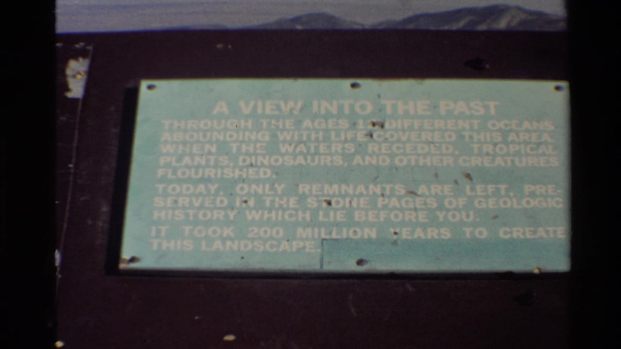1980 8mm frame of a green geologic-history plaque titled A View Into The Past at an outdoor Western USA scenic stop.